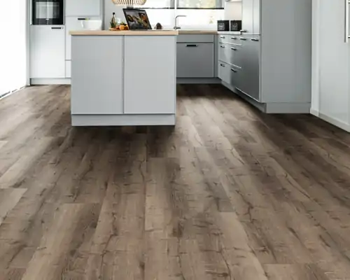 Moderne Küche mit hellgrauen Schränken und Arbeitsinsel, dunkler lebendiger Eiche-Designboden in einer Küche vom Schreiner, helle Wände und Fenster im Hintergrund.