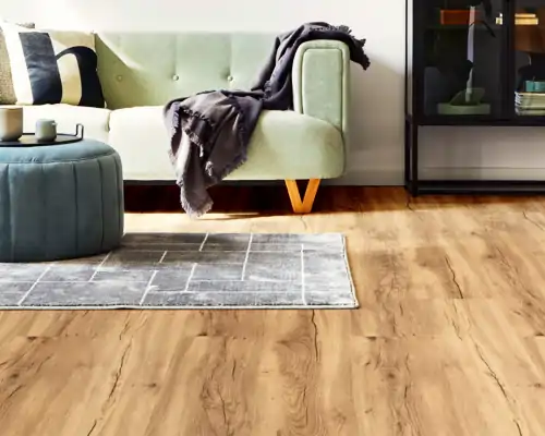 Heller, grüner Samtsofa mit Holzfüßen, graue Decke darauf, blauer runder Hocker, grauer Teppich auf Designboden Eiche lebhaft vom Schreiner mit natürlicher Holzmaserung im Wohnzimmer