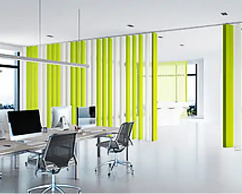 Ein modernes Büro mit MHZ Lamellenvorhängen in gelb-weißen Streifen. Das Büro ist minimalistisch eingerichtet mit Schreibtischen und Stühlen, und es gibt große Fenster, die viel Tageslicht hereinlassen.