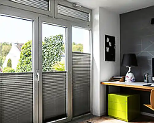 Moderner Indoor Sonnenschutz mit MHZ Plissee an bodentiefen Fenstern in einem Homeoffice.
