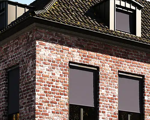 Ziegelhaus mit mehreren großen Fenstern, an denen dunkle MHZ Außenrollos als Sonnenschutz angebracht sind.