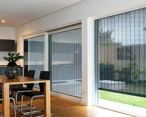 Modernes Esszimmer mit großen Glasfronten, an denen dunkle, fein strukturierte Metallbehänge von MHZ als Sonnenschutz angebracht sind.