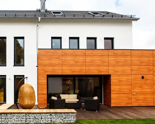 Moderne Terrasse mit Holzbelag, Gabionenbank und stilvoller Outdoor-Sitzgruppe vor einem Einfamilienhaus mit Holzfassade