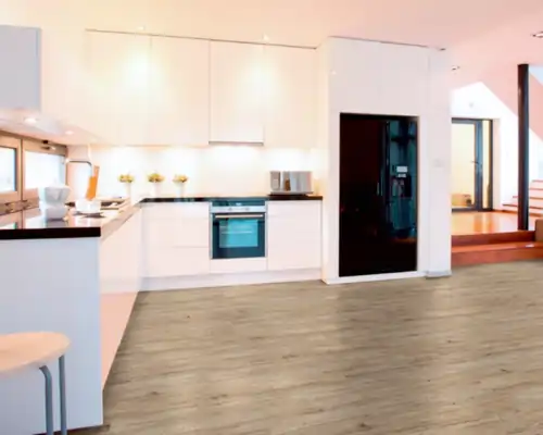 Moderne weiße Küche mit schwarzen Arbeitsflächen und eingebautem Ofen, heller Vinylboden mit Holzmaserung, offene Raumgestaltung mit Treppe im Hintergrund.