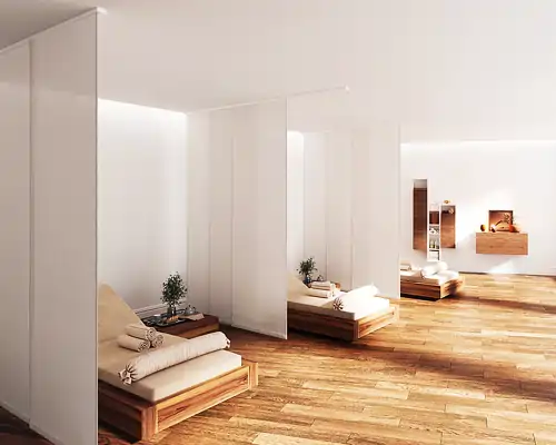 Mehrere MHZ Flächenvorhänge in Weiß trennen einzelne Liegeflächen in einem Raum. Jede Liegefläche besteht aus einem niedrigen Holzrahmen mit einer hellen Matratze und einem zusammengerollten Handtuch. Auf kleinen Beistelltischen neben den Liegen stehen Pflanzen. Der Boden ist aus hellem Holz, die Wände sind weiß und schlicht gehalten.