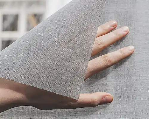 Hand hält ein graues, halbtransparentes Hafttextil namens SQUID von MHZ, das sich fein gewebt zeigt und sich flexibel biegen lässt.