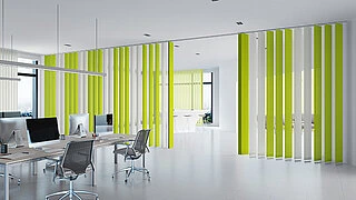Büro mit mehreren Arbeitsplätzen, ausgestattet mit MHZ Lamellenvorhängen als Raumteiler in hellgrüner und weißer Farbgebung. Die Lamellen sind vertikal angeordnet und reichen vom Boden bis zur Decke. Schreibtische mit Computern und Bürostühlen sind vor den Vorhängen platziert. Große Fenster lassen Tageslicht in den Raum.