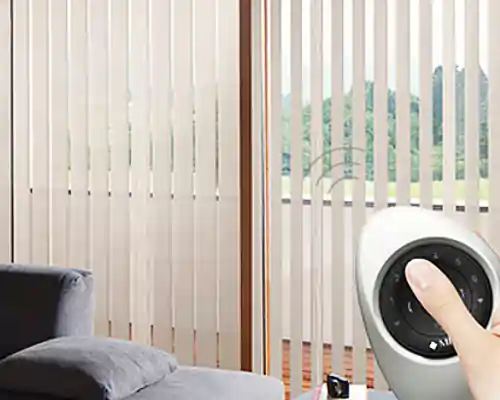 Beigefarbener MHZ Lamellenvorhang vor einer großen Fensterfront, im Vordergrund eine Hand, die eine runde Fernbedienung für Sart-Home mit mehreren Tasten hält, links ein graues Sofa mit Kissen.