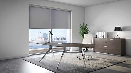 Modernes Büro mit MHZ Rolo Sonnenschutz in Grau vor großen Fenstern, Schreibtisch mit Lampe, Bürostuhl, Sideboard und Pflanze.