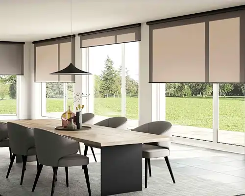 Esszimmer mit großem Holztisch und sechs gepolsterten Stühlen mit schwarzen Beinen. An den großen Fenstern hängen beigefarbene MHZ Rollos, die teilweise heruntergelassen sind. Über dem Tisch hängt eine schwarze, flache Pendelleuchte. Draußen ist eine grüne Wiese mit Bäumen zu sehen.