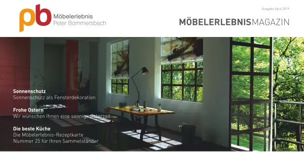 Moderner Schreibtisch mit Holzplatte und schwarzem Gestell vor großen Fenstern mit grüner Pflanzenansicht, daneben Stehlampe und Stuhl, Tageslicht fällt ein.