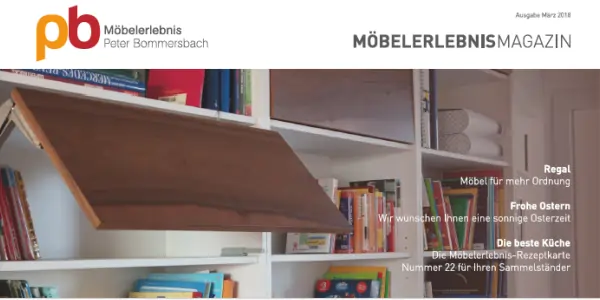 Offenes Wandregal mit Klapptür aus Nußbaum Holz, gefüllt mit Büchern und Ordnern, im Hintergrund weitere Regale mit Büchern.