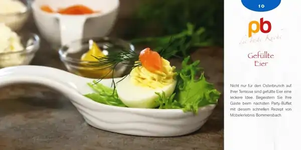 Gefülltes Ei mit Dill und Lachs auf grünem Salat in weißer Schale, im Hintergrund Schälchen mit Senf und weiteren Zutaten.
