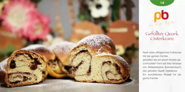 Gefüllter Quark-Osterkranz mit Puderzucker bestäubt, angeschnitten und auf einem Teller serviert, im Hintergrund unscharfe Osterdekoration.
