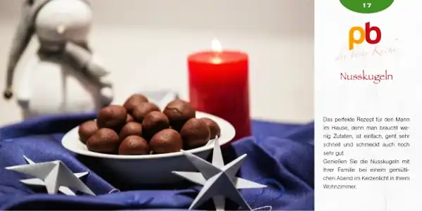 Eine Rezeptkarte mit dem Titel 'Nusskugeln' und dem Logo 'pb die beste Küche' oben. Rechts steht ein kurzer Text, der das Rezept beschreibt: Es ist einfach, benötigt wenige Zutaten, geht schnell und schmeckt gut. Links im Bild steht eine blaue Schale mit vielen runden, braunen Nusskugeln. Im Hintergrund ist eine rote Kerze und eine weiße Papierstern-Dekoration zu sehen. Weiter hinten steht eine kleine Astronautenfigur, unscharf dargestellt.