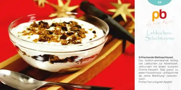 Eine Dessertschale mit einer Schicht weißer Creme, die mit zerbröselten Lebkuchenstücken bestreut ist. Die Schale steht auf einem roten Untergrund, im Hintergrund sind goldene Sterne und ein Holzstößel zu sehen. Rechts neben der Schale ist ein Teil eines Etiketts mit dem Schriftzug 'pb die beste Küche' und 'Lebkuchen-Schichtcreme' zu erkennen. Darunter steht ein kurzer Text, der die Creme als festlich-weihnachtliches Dessert beschreibt.