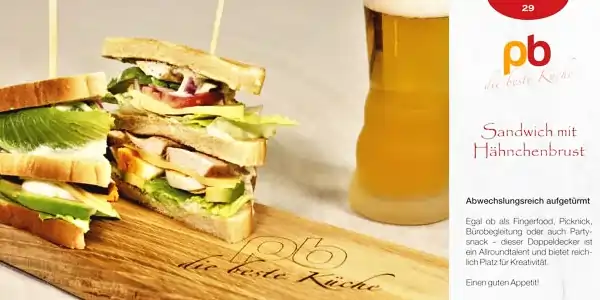 Zwei übereinander gestapelte Sandwichhälften mit Hähnchenbrust, Salat, Tomate und Gurke auf Toastbrot. Im Hintergrund steht ein Glas mit einem hellen Getränk. Rechts daneben befindet sich ein Textblock mit dem Logo "pb die beste Küche" und der Überschrift "Sandwich mit Hähnchenbrust". Darunter steht ein kurzer Beschreibungstext, der das Sandwich als abwechslungsreich und vielseitig beschreibt, geeignet für Fingerfood, Picknick, Bürotätigkeit oder Partybuffet.