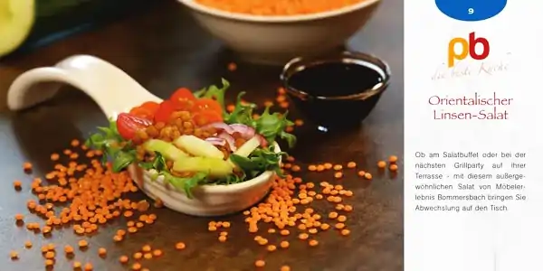 Auf einem weißen Löffel liegt ein Salat aus roten Linsen, grünen Salatblättern, Tomatenstücken, roten Zwiebelringen und Avocadoscheiben. Im Hintergrund steht eine kleine Schale mit dunkler Soße und eine weitere Schale mit einer orangefarbenen Suppe. Rechts daneben ist ein Teil einer Rezeptkarte mit dem Titel 'Orientalischer Linsen-Salat' zu sehen.