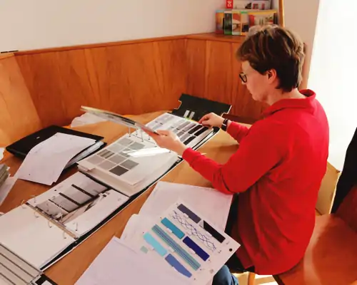 Mitarbeiterin der Schreinerei Möbelerlebnis Bommersbach in Schongau bei der Beratung mit Musterkatalogen für verschiedene Sonnenschutzlösungen wie Plissees, Rollos, Jalousien und Markisen bzw. Sonnensegel.