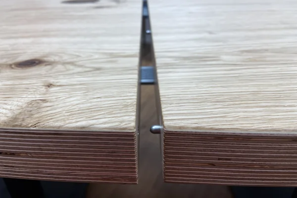 Nahaufnahme zweier Holzplatten mit sichtbarer Schichtstruktur, die durch eine Metallsteckverbindung verbunden werden.