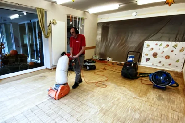 Fachkraft schleift einen Parkettboden mit Bodenschleifmaschine bei der Renovierung